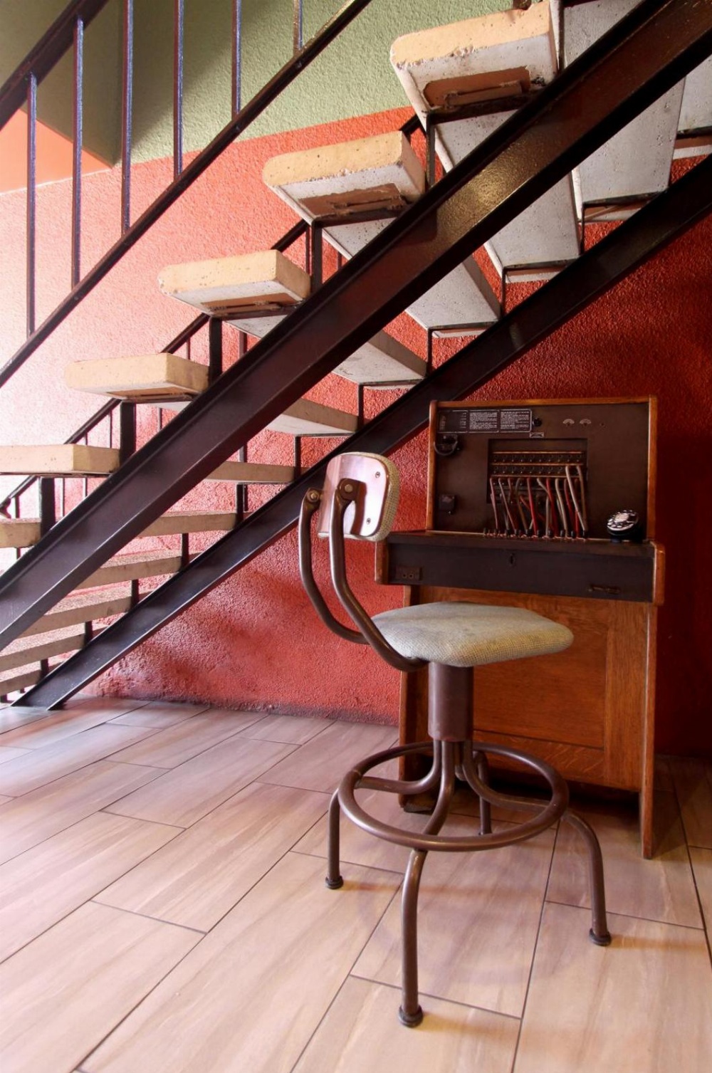 A staircase with a stool and telephone in front of a red wall.